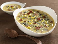 two bowls of soup with corn and other toppings on a table next to a spoon