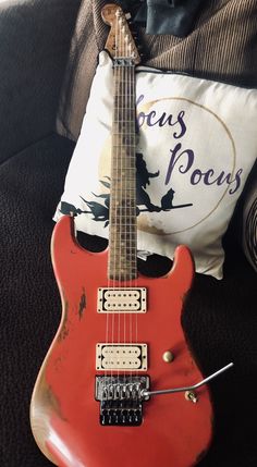 an old red electric guitar sitting on top of a couch next to a throw pillow