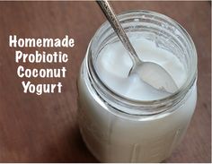 a glass jar filled with yogurt sitting on top of a wooden table next to a spoon