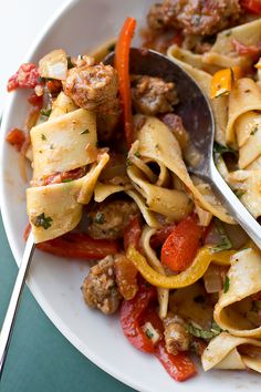 a white plate topped with pasta and meat covered in tomato sauce next to a fork