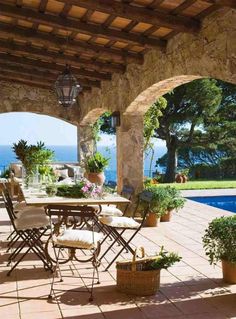 an outdoor dining table with chairs and potted plants next to a swimming pool in the background