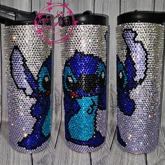 three tumbles decorated with blue and silver sequins on wooden boards, one is holding a toothbrush