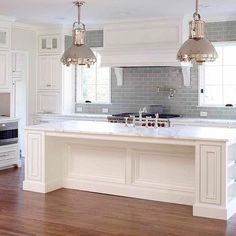 a kitchen with white cabinets and marble counter tops, an island in the middle is flanked by two pendant lights