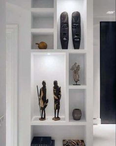 several african masks on shelves in a white room