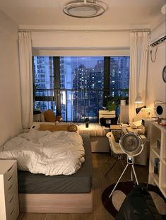 a bedroom with a bed, desk and window overlooking the cityscape at night