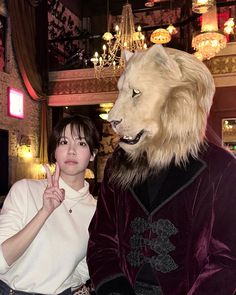 a woman standing next to a man in a lion costume at a restaurant with chandeliers hanging from the ceiling