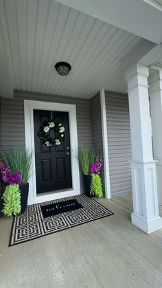 a black door and some purple flowers on the front porch with white trimmings