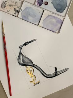 a pair of high heeled shoes sitting on top of a table next to paintbrushes