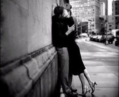 a man and woman leaning against a wall on the sidewalk in front of tall buildings