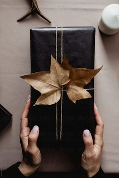 a woman holding a present wrapped in brown paper with leaves on it by julia radwig for stockstations