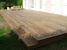 a large wooden deck in the middle of a yard with chairs and trees behind it