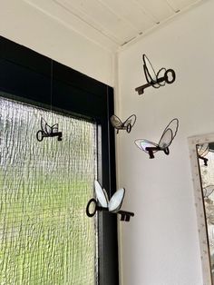 three wrought iron butterflies hang on the wall next to a window with green grass in the background