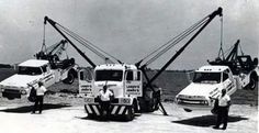 three trucks are parked next to each other in front of a crane and two men