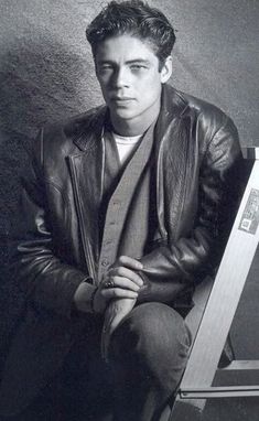 a black and white photo of a man in a leather jacket sitting on a chair