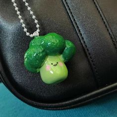 a green broccoli necklace is hanging from a black leather bag on a chain