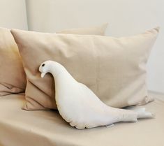 a white bird sitting on top of a bed next to two pillows