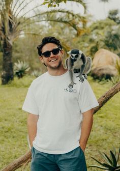 a man is holding a small monkey on his shoulder in front of trees and grass