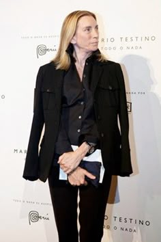 a woman standing in front of a white wall with a black jacket on it's back