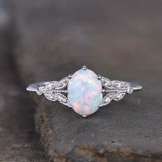 a white opal and diamond ring sitting on top of a rock