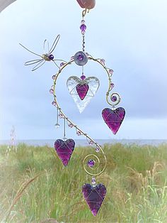 a wind chime with hearts hanging from it's side in the grass next to an open field