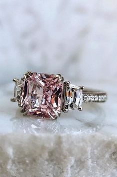 a pink diamond ring with three baguettes in the center on a marble surface