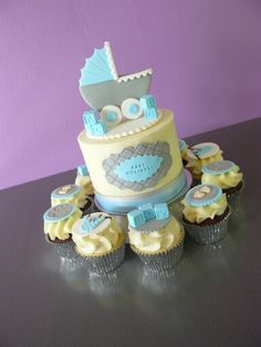 a baby shower cake surrounded by cupcakes on a black table with purple wall in the background