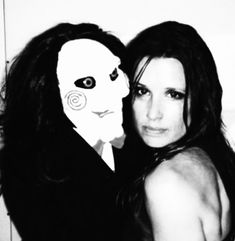 a woman posing with a creepy mask on her face next to a man in a suit