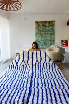 a woman sitting on top of a bed under a blue and white striped blanket in a room