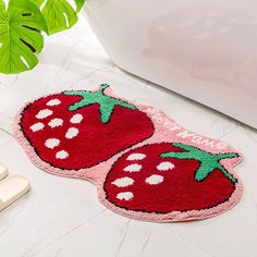 two strawberry shaped rugs sitting on the floor next to a bathtub and slippers