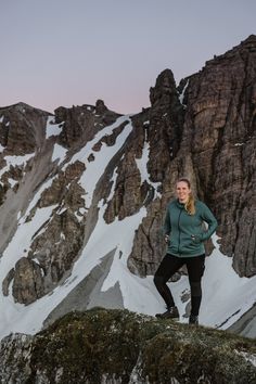 a woman standing on top of a snow covered mountain next to a large rock formation