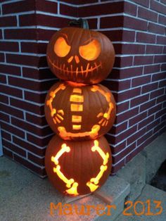 three carved pumpkins sitting on top of each other in front of a brick wall