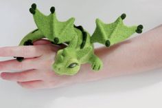 a hand is holding a green dragon brooch on it's left arm,