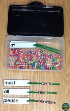 some beads are in a plastic container on a wooden table with labels and magnets