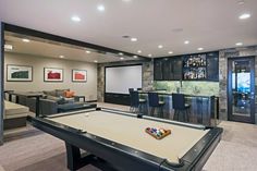 a game room with a pool table, bar and couches in front of a projector screen