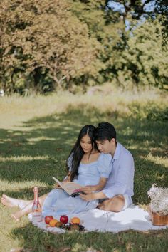 a man and woman are sitting on the grass with an open book in their hands