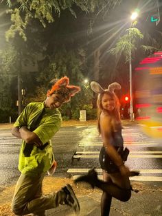 two people in costumes are running across the street at night, with one person wearing bunny ears on his head