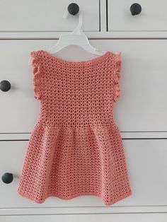 a pink crocheted dress hanging on a white dresser