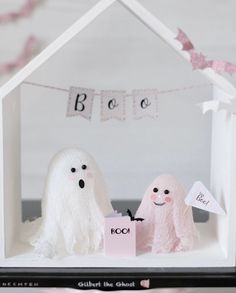 two white ghost figurines in front of a house with the word boo written on it