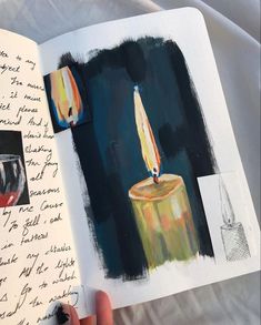 a hand holding an open book with two lit candles on the cover and writing in it