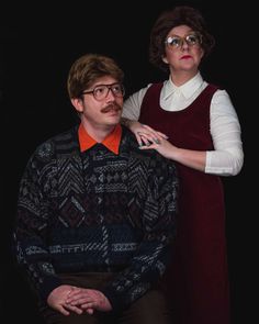 a man and woman standing next to each other in front of a black background wearing glasses