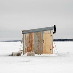 an outhouse in the middle of nowhere with snow on the ground and trees behind it