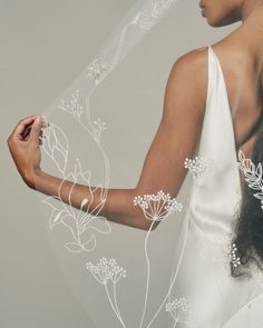 a woman in a white dress holding a veil over her shoulder with flowers on it