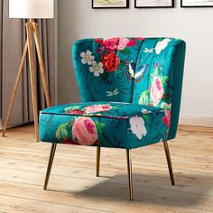 a blue chair with flowers on it sitting in front of a lamp and pictures hanging on the wall