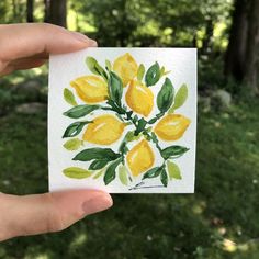 a person holding up a piece of paper with watercolor paint on it that has yellow flowers and green leaves