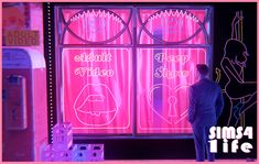 a man standing in front of a neon pink window with writing on the windows and behind it is an advertisement for a video game