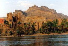 an old castle sits on the shore of a lake in front of palm trees and mountains