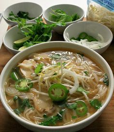 a bowl of soup with noodles, vegetables and herbs in it on a wooden table