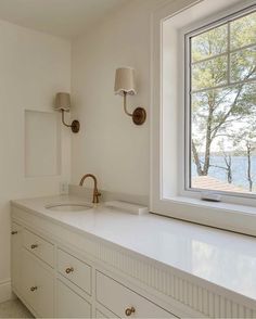 a white bathroom with two sinks and a large window in the wall above it,