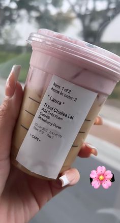 a hand holding a cup of coffee in front of a window with a pink flower