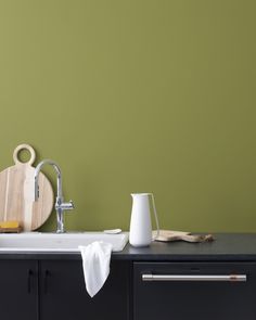 a kitchen with green walls and white counter tops, including a black cabinet holding utensils